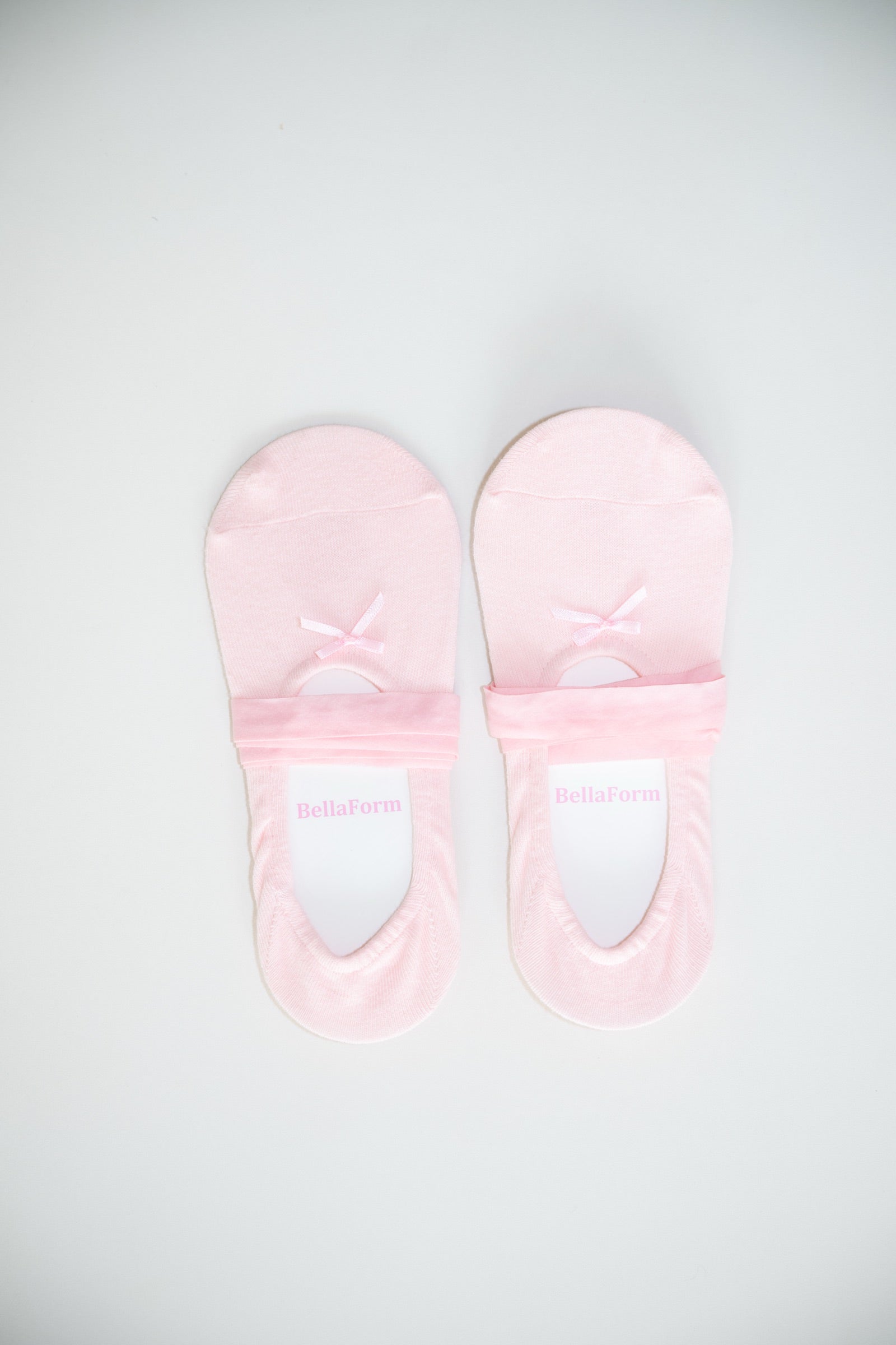 A pair of BellaForm ballet-laced grip socks in Ballet Pink, laid flat on a pale background with satin ribbons wrapped around the arch.