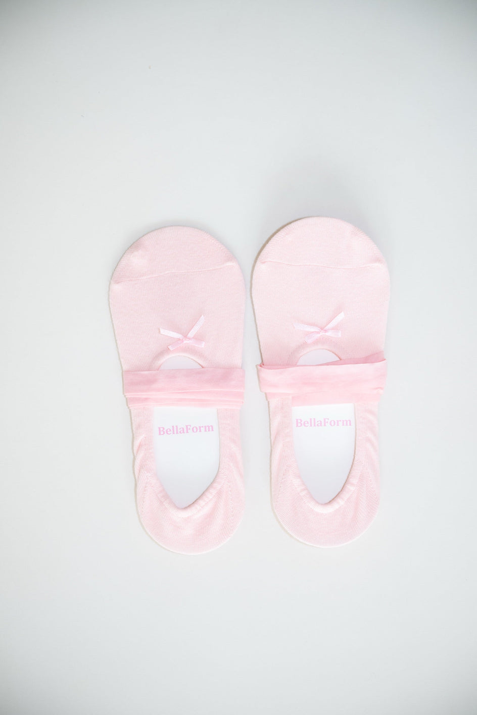 A pair of BellaForm ballet-laced grip socks in Ballet Pink, laid flat on a pale background with satin ribbons wrapped around the arch.