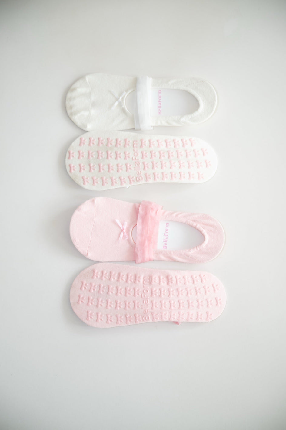 BellaForm grip socks in both colorways side by side, Ballet Pink and Cloud White, showing the knit top and the bow-print silicone sole of each.