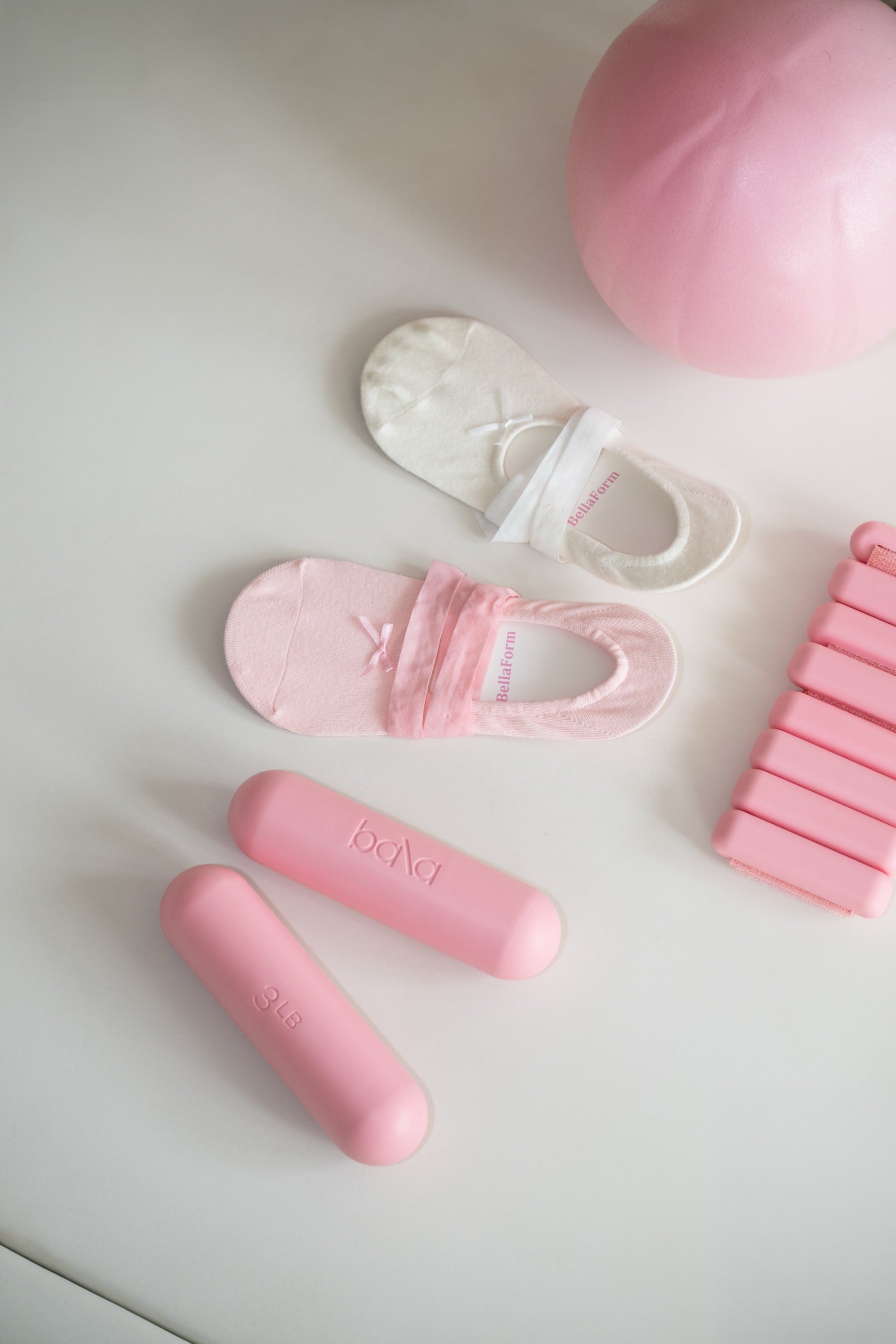 Flat lay of BellaForm grip socks with hand weights and a small pink Pilates ball on a neutral background.